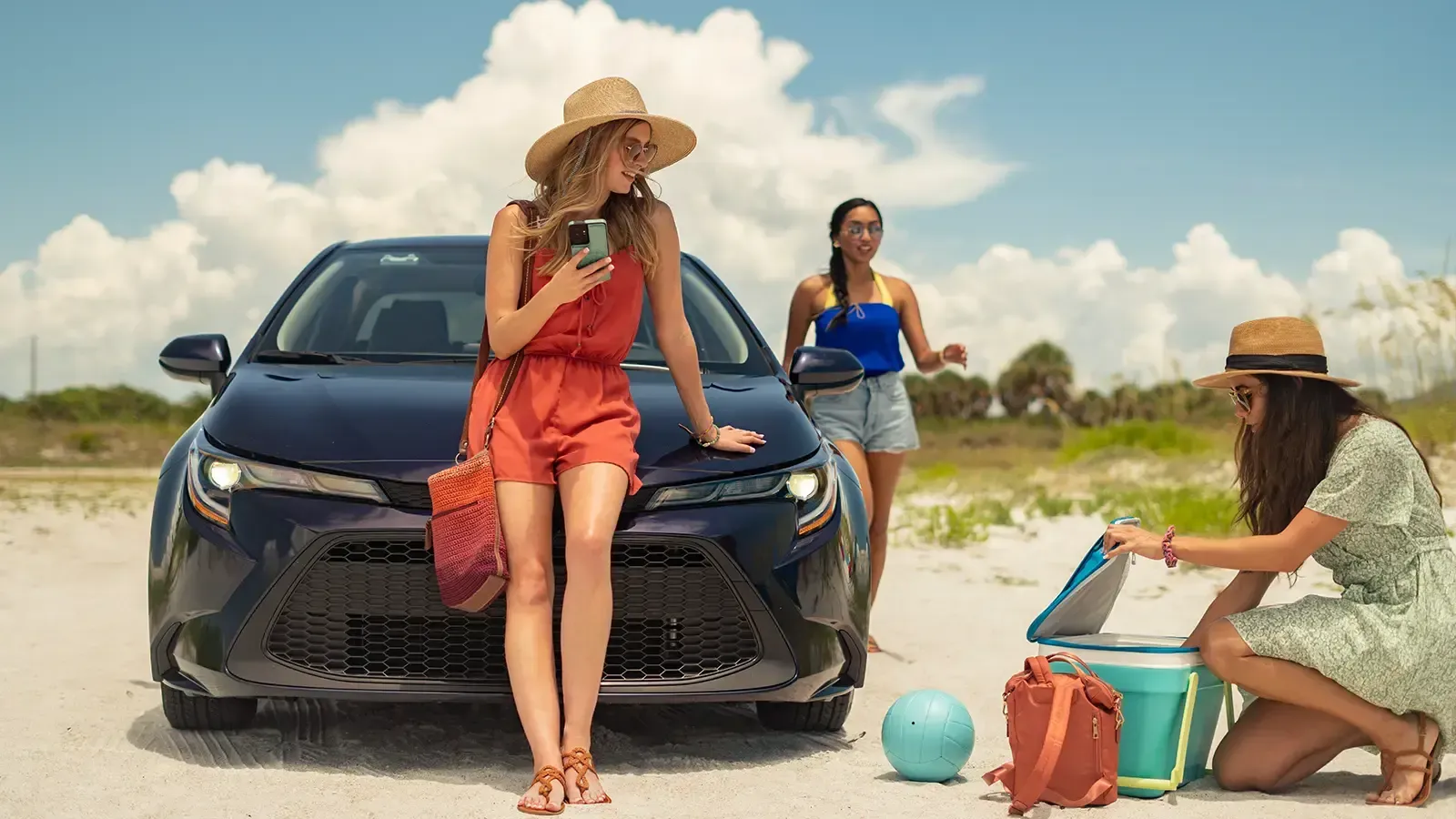 sunny day on the beach women hanging out next to hybrid car