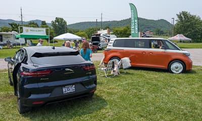 Vista trasera de tres cuartos de un SUV negro y una van vintage naranja y blanca en un evento de vehículos eléctricos al aire libre.