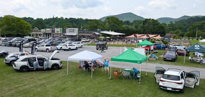 Vista amplia de un evento de EV al aire libre con filas de autos, carpas blancas y verdes, y personas bajo toldos.