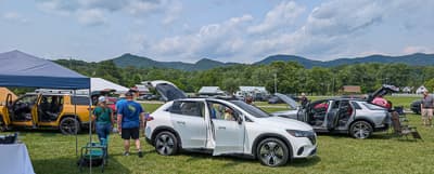 Vista lateral de una SUV eléctrica blanca con las puertas abiertas en una exhibición al aire libre de EV.
