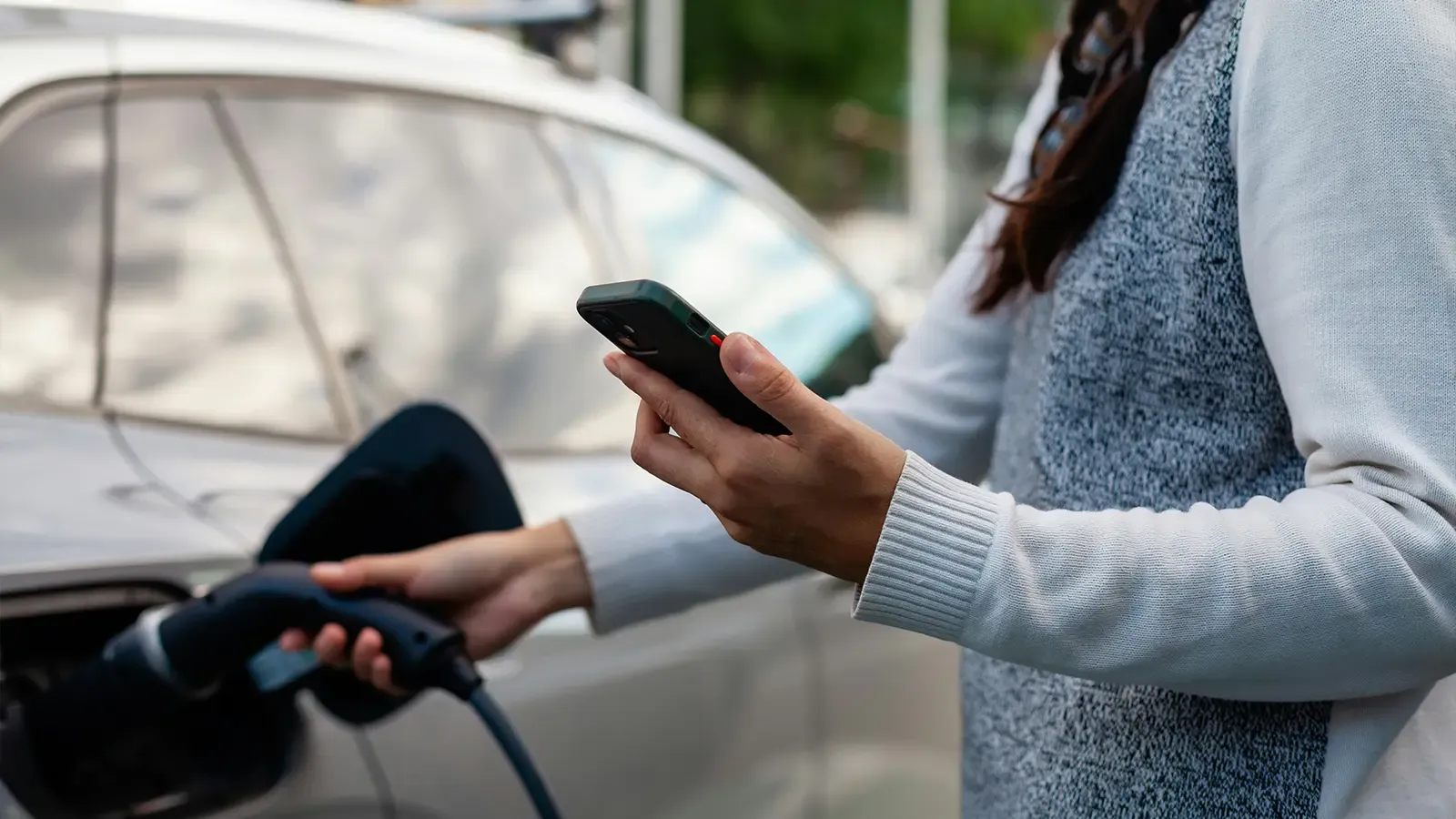 A women charging her EV in afternoon sunlight