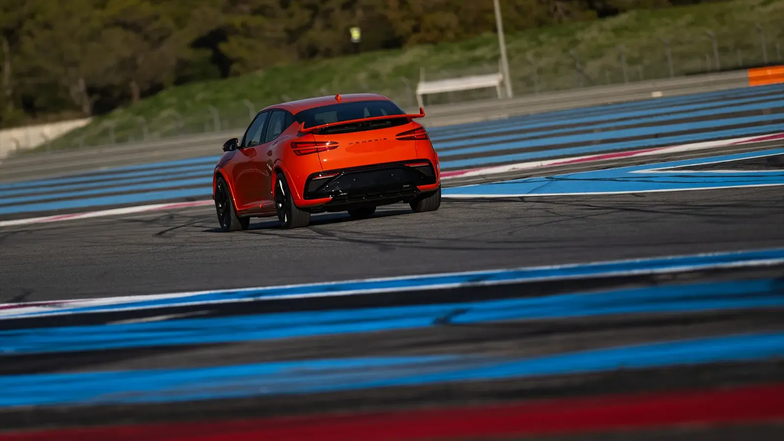 A 2027 Orange Genesis GV60 Magma rear view on a racetrack