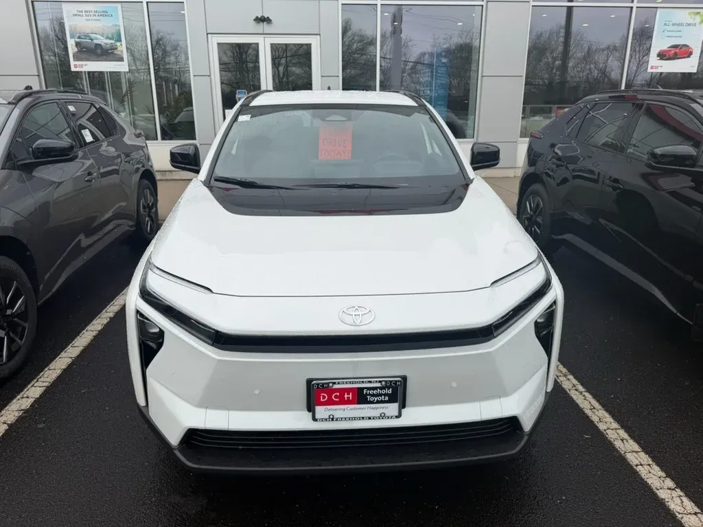 Front view of a white Toyota bZ parked between two dark SUVs at a dealership.