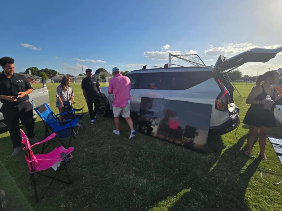 Vista trasera de tres cuartos de una Kia EV9 blanca con la cajuela abierta en un evento en un campo de fútbol.