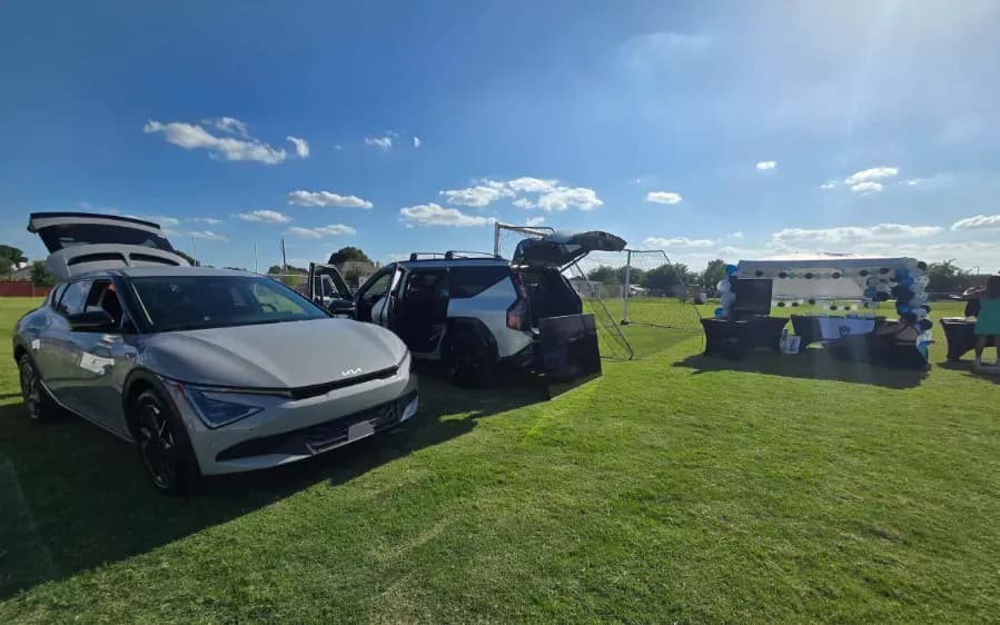 Vista frontal de un Kia EV6 plateado y un EV9 con las compuertas traseras abiertas en un campo de soccer.