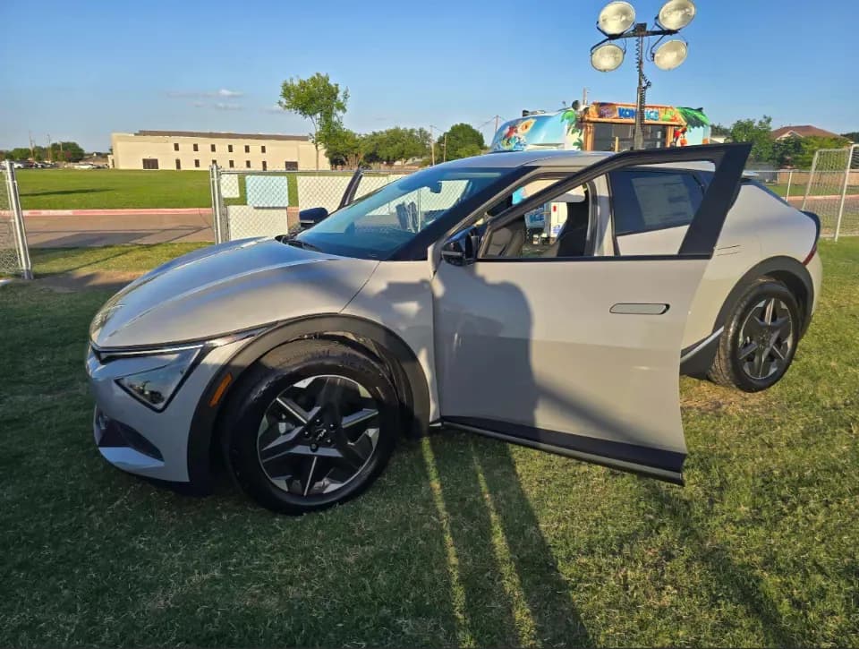 Un Kia EV6 plateado con la puerta del conductor abierta en un campo de césped.