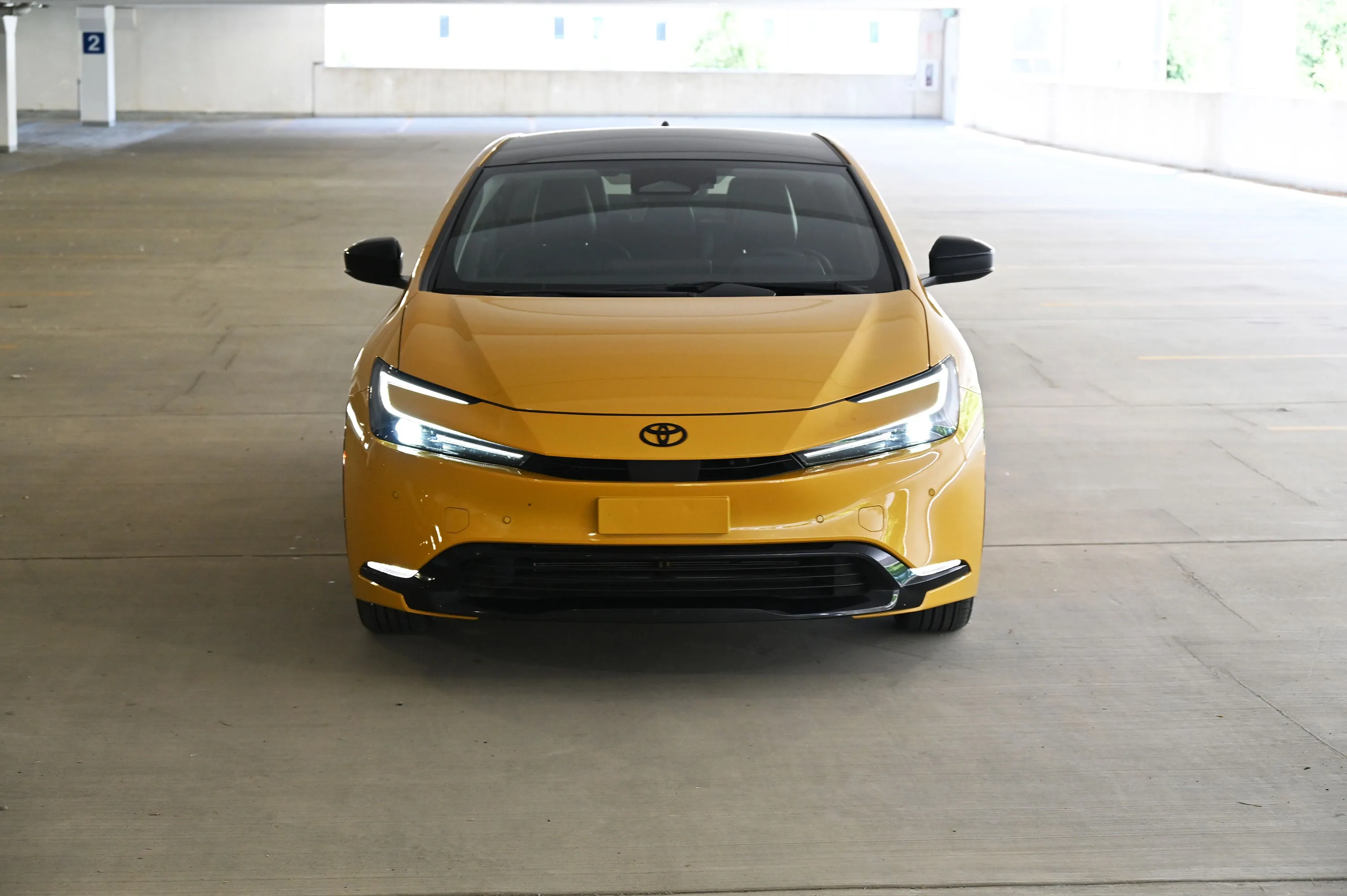 Front view of a yellow Toyota Prius with headlights on in a parking garage.