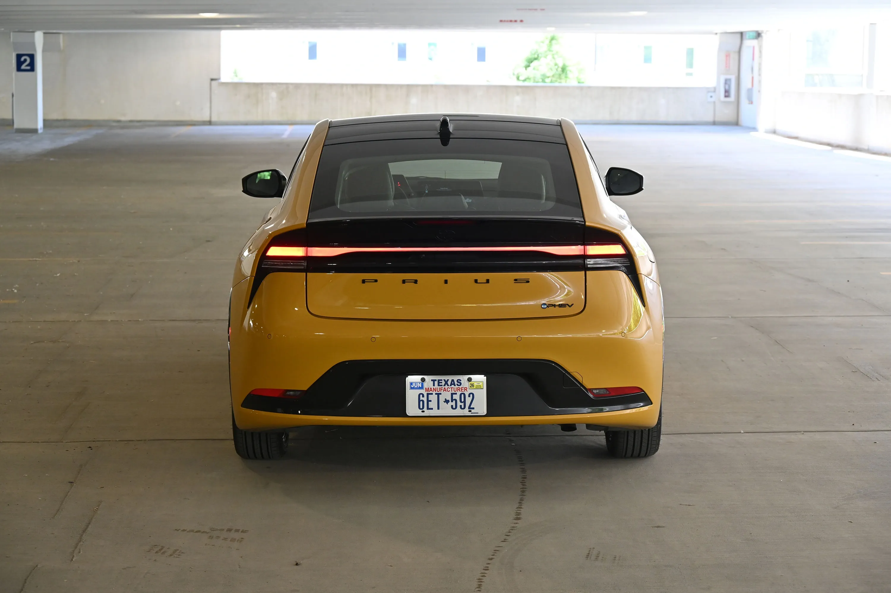 Rear view of a yellow Toyota Prius with a black roof in a parking garage.
