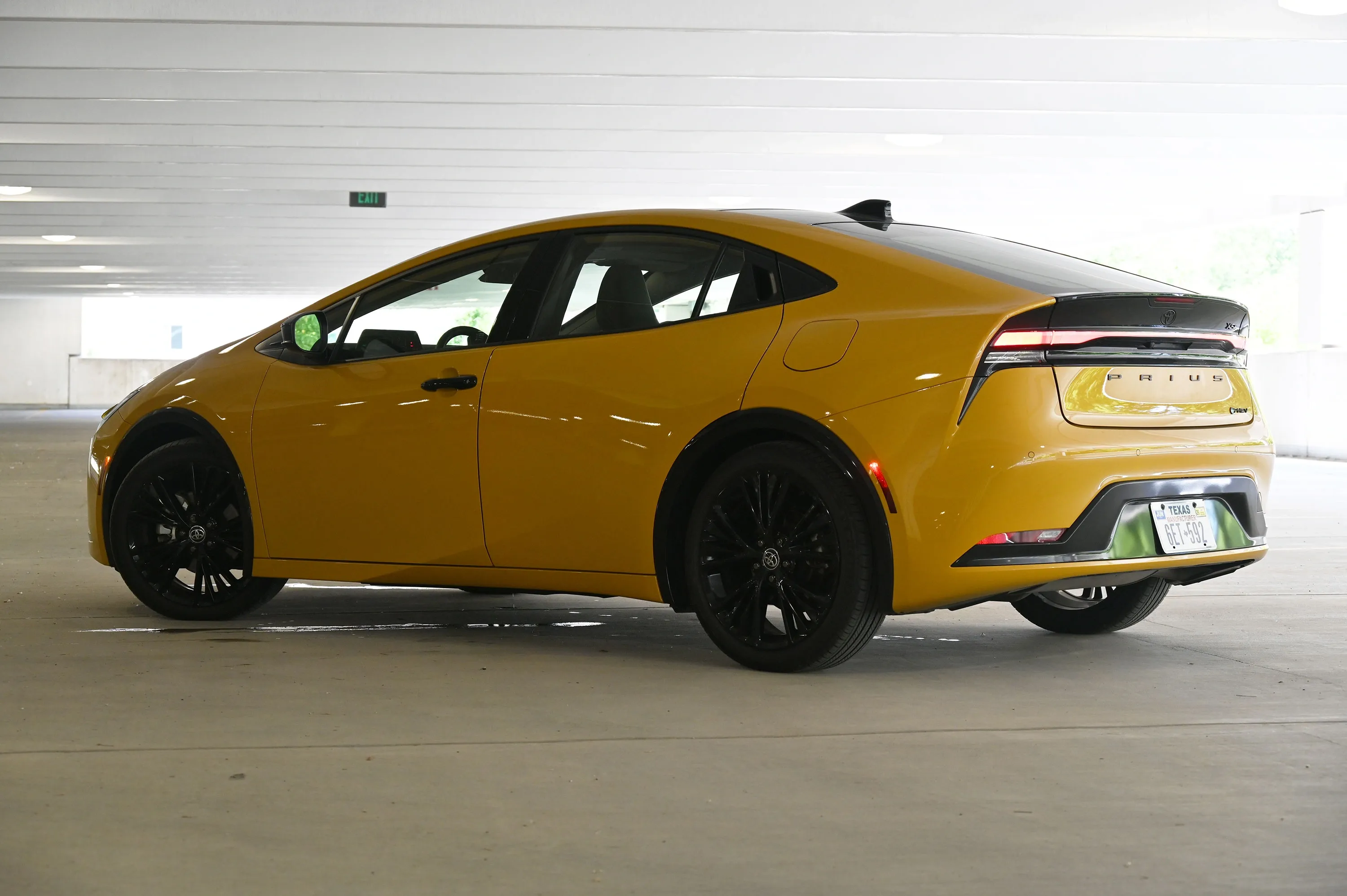 Rear three-quarter view of a yellow Toyota Prius with black wheels and a black roof.