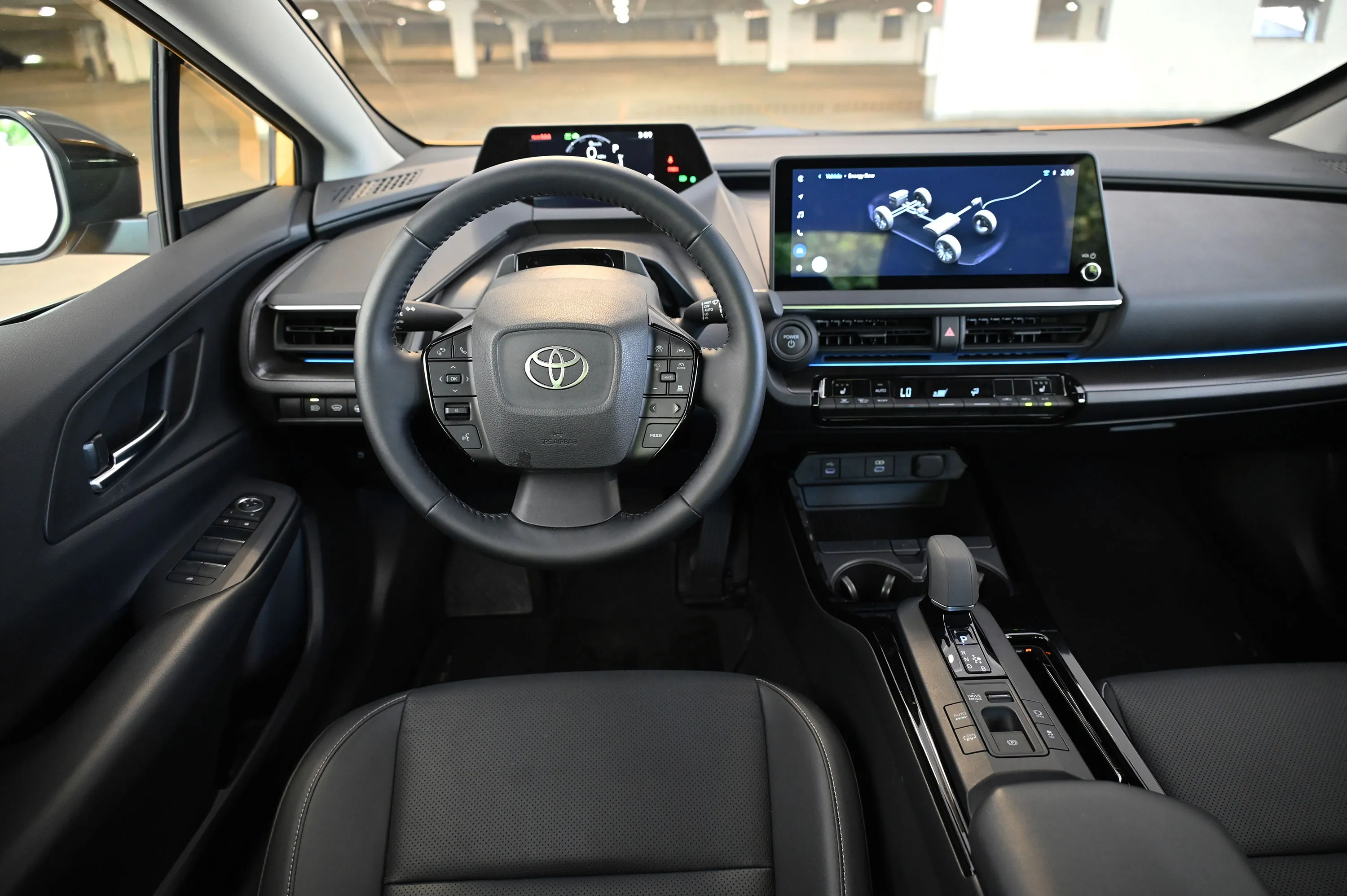 Toyota Prius cockpit with steering wheel, digital display, and center touchscreen showing the hybrid system.
