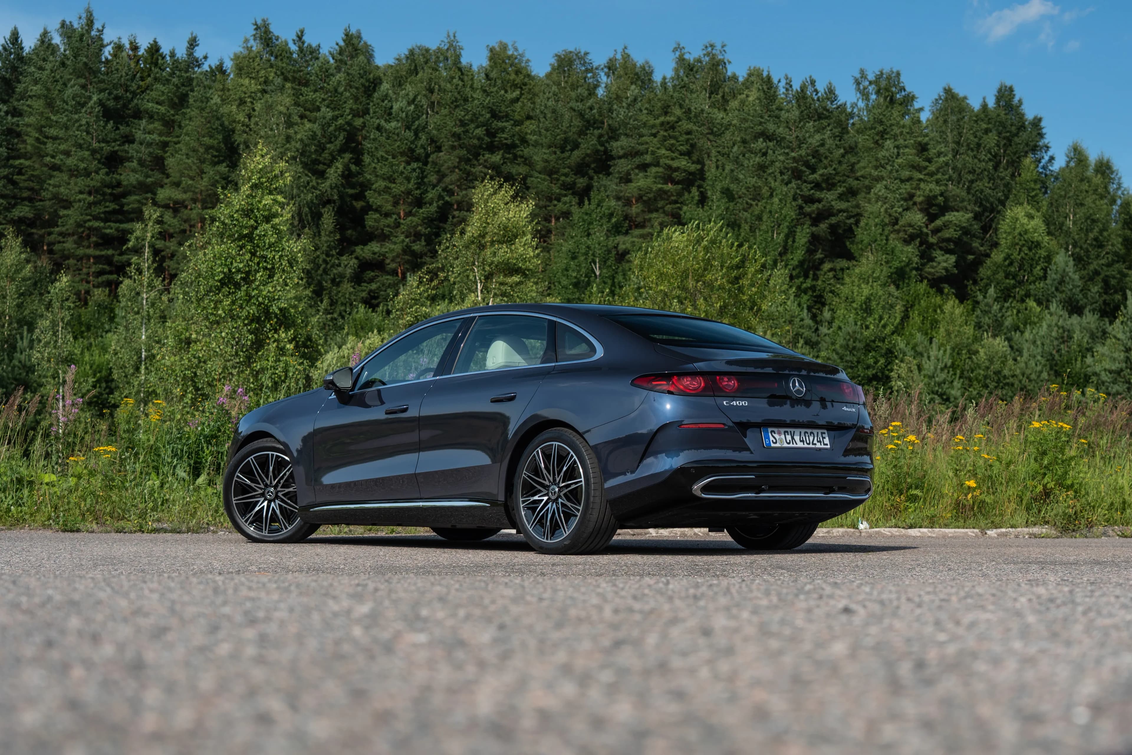 Vista trasera de tres cuartos de un sedán eléctrico Mercedes-Benz C-Class oscuro estacionado junto a un camino boscoso.