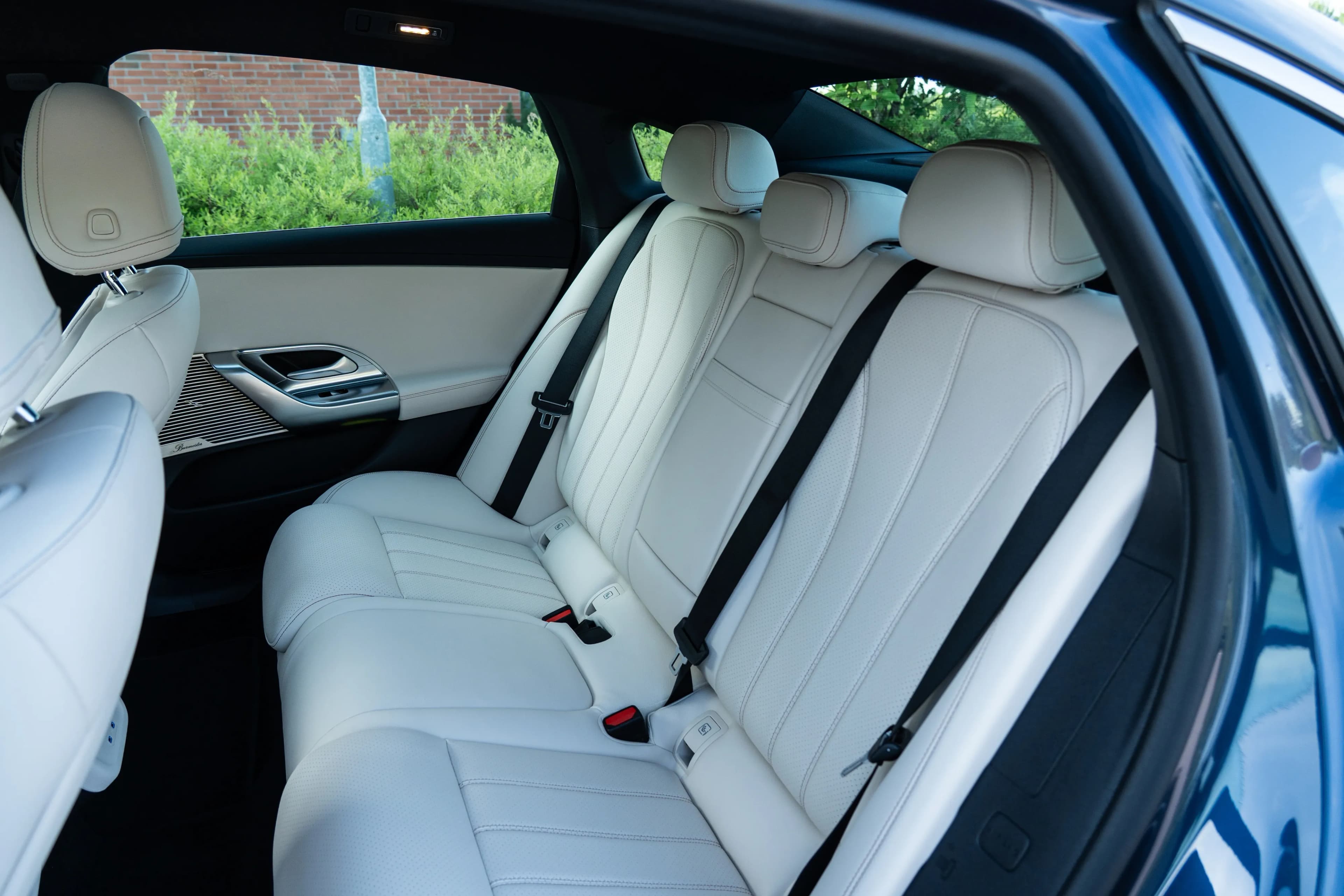 Interior del asiento trasero con asientos de cuero blanco y marco de puerta azul.