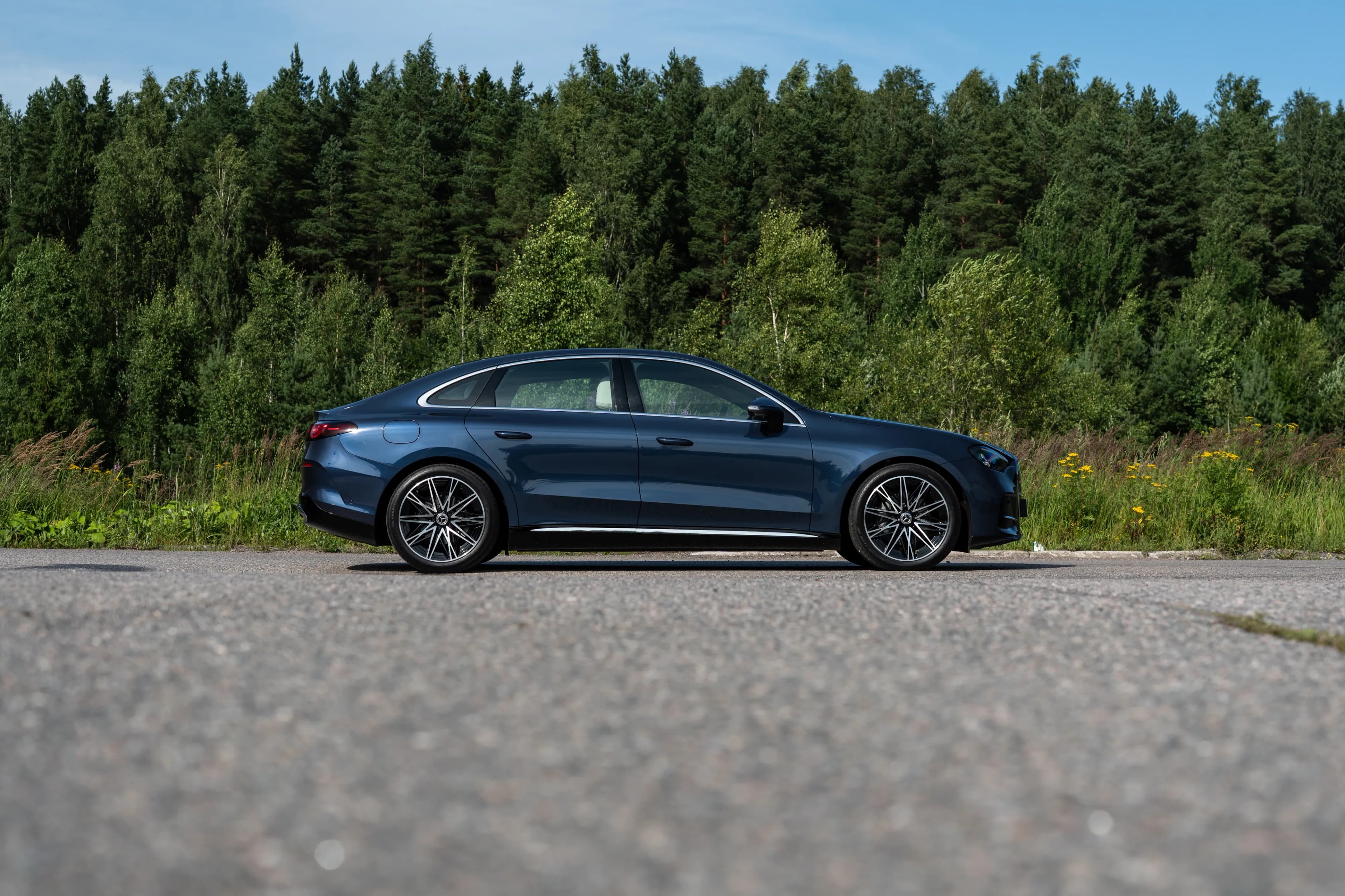 Perfil lateral de un sedán eléctrico Mercedes-Benz C-Class azul oscuro junto a una carretera.