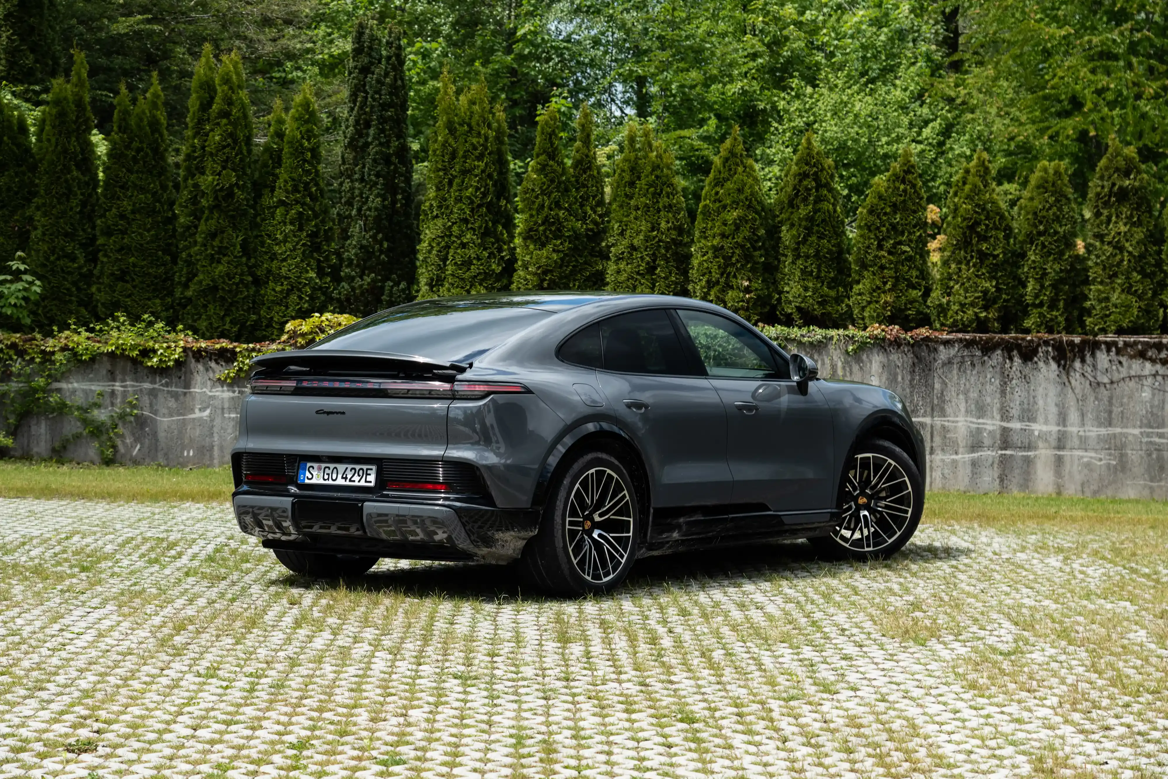 Vista trasera de tres cuartos de un Porsche Cayenne Coupe Electric gris estacionado en una entrada de adoquines.