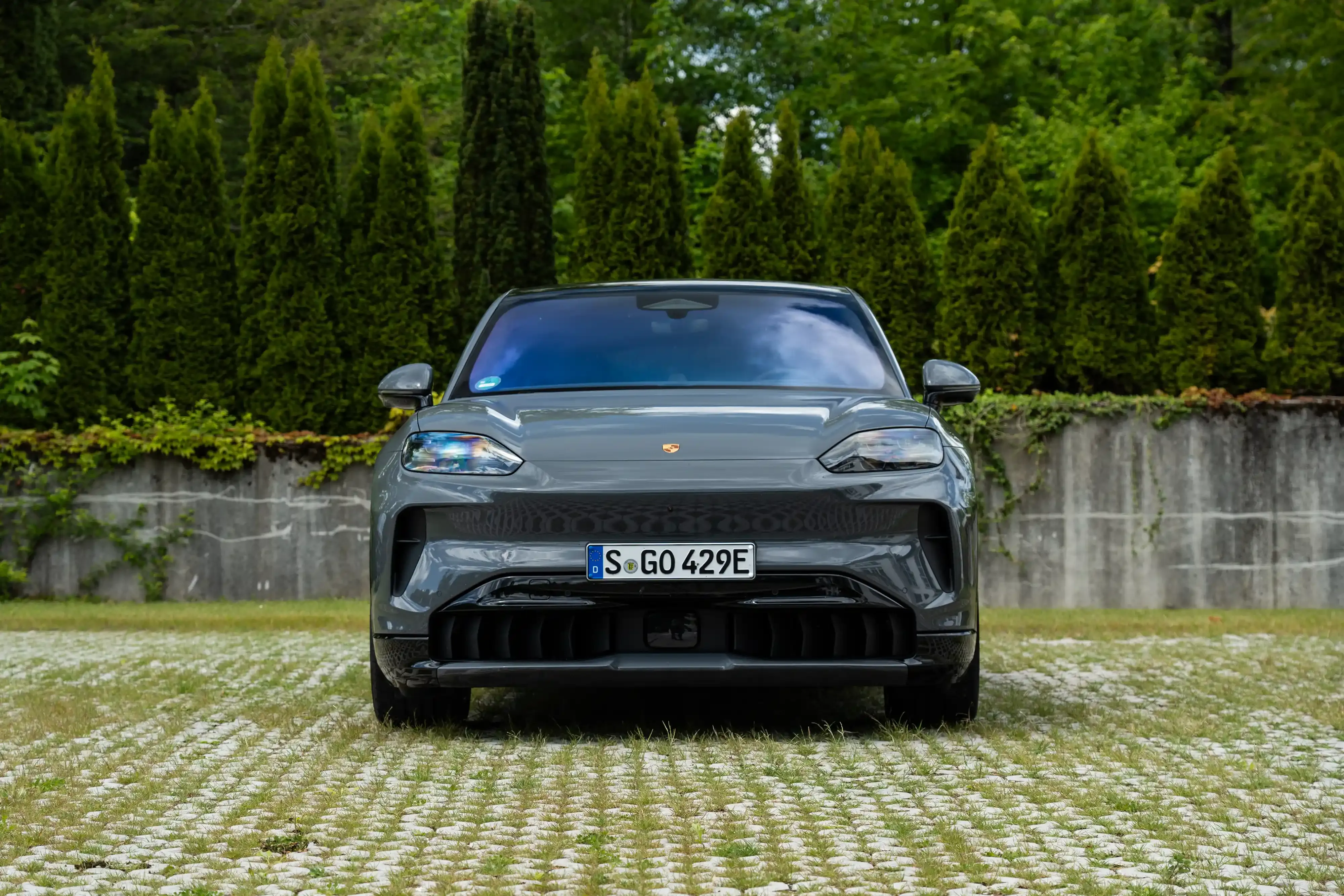 Vista frontal de un Porsche Cayenne Coupé Electric gris estacionado en una entrada de piedra.