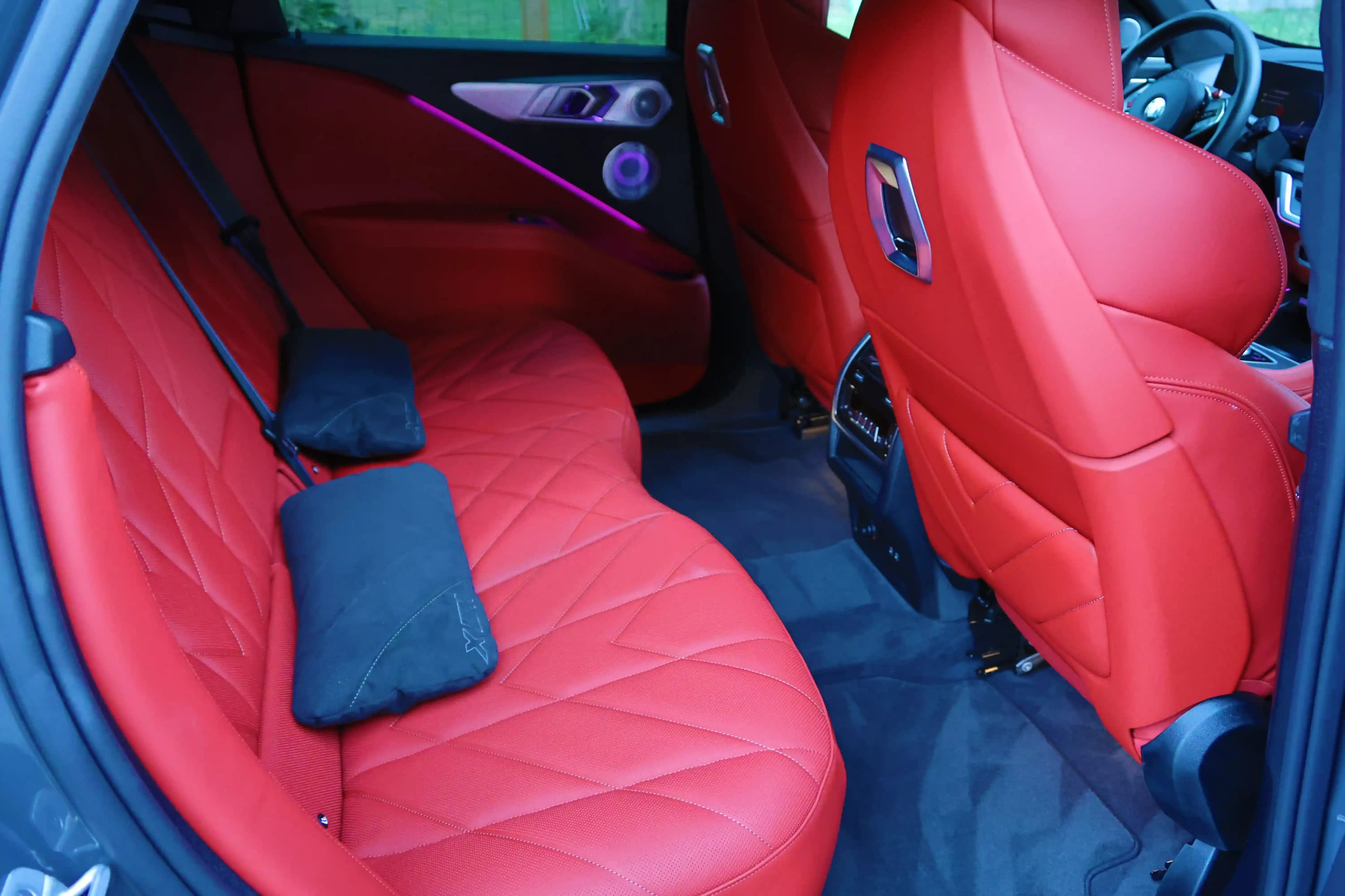 Rear-seat interior with red quilted leather seats, ambient lighting, and the front cabin visible ahead.