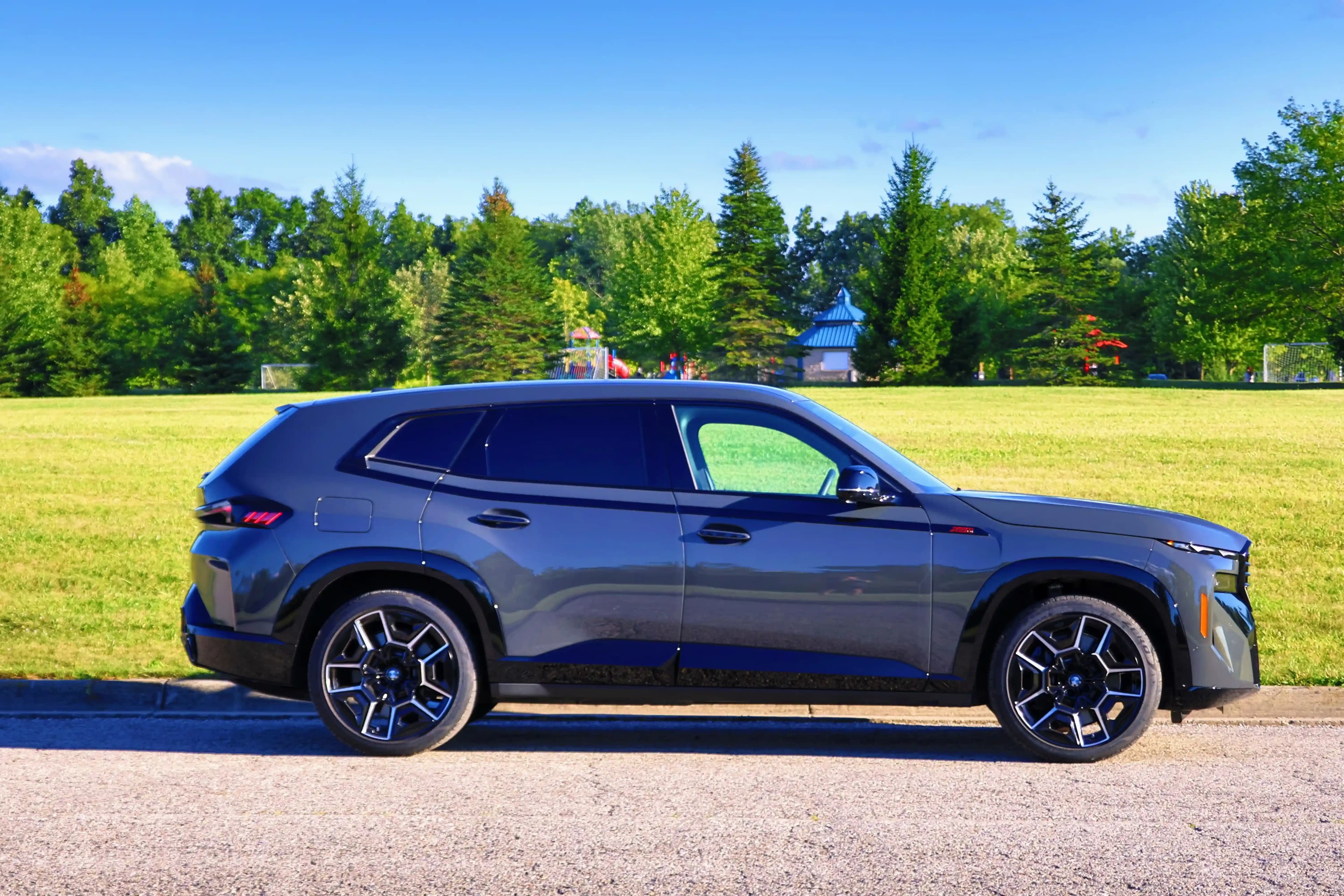 Side profile of a gray BMW XM SUV parked beside a grassy field.