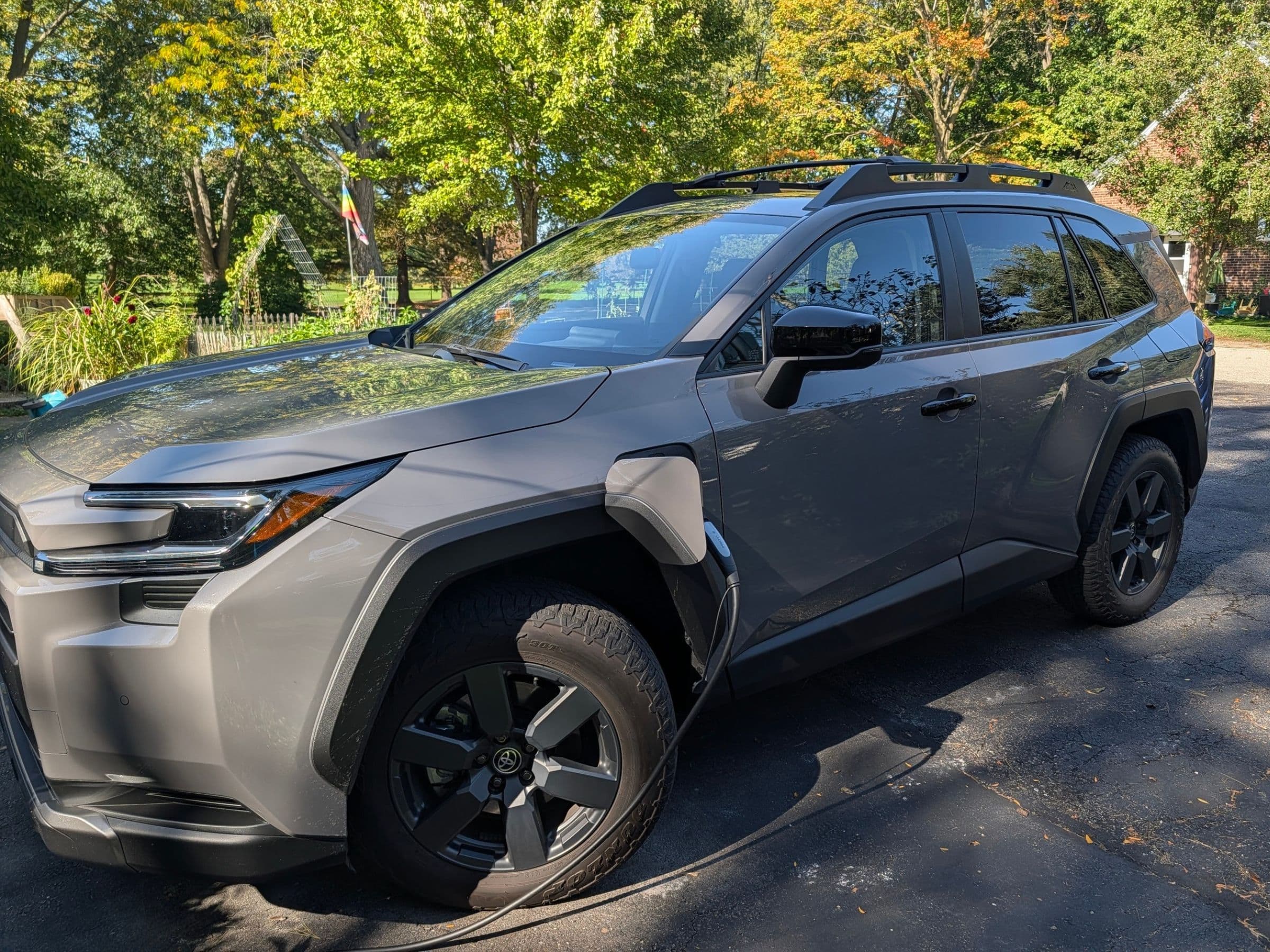 Grey Toyota RAV4 PHEV charging beside a home in front of a green garden in background.
